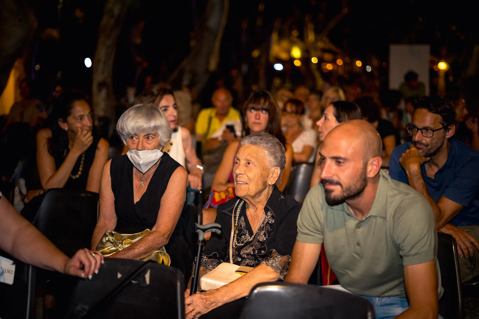 Il pubblico seduto e attento verso il palco, con una spettatrice con la mascherina in primo piano
