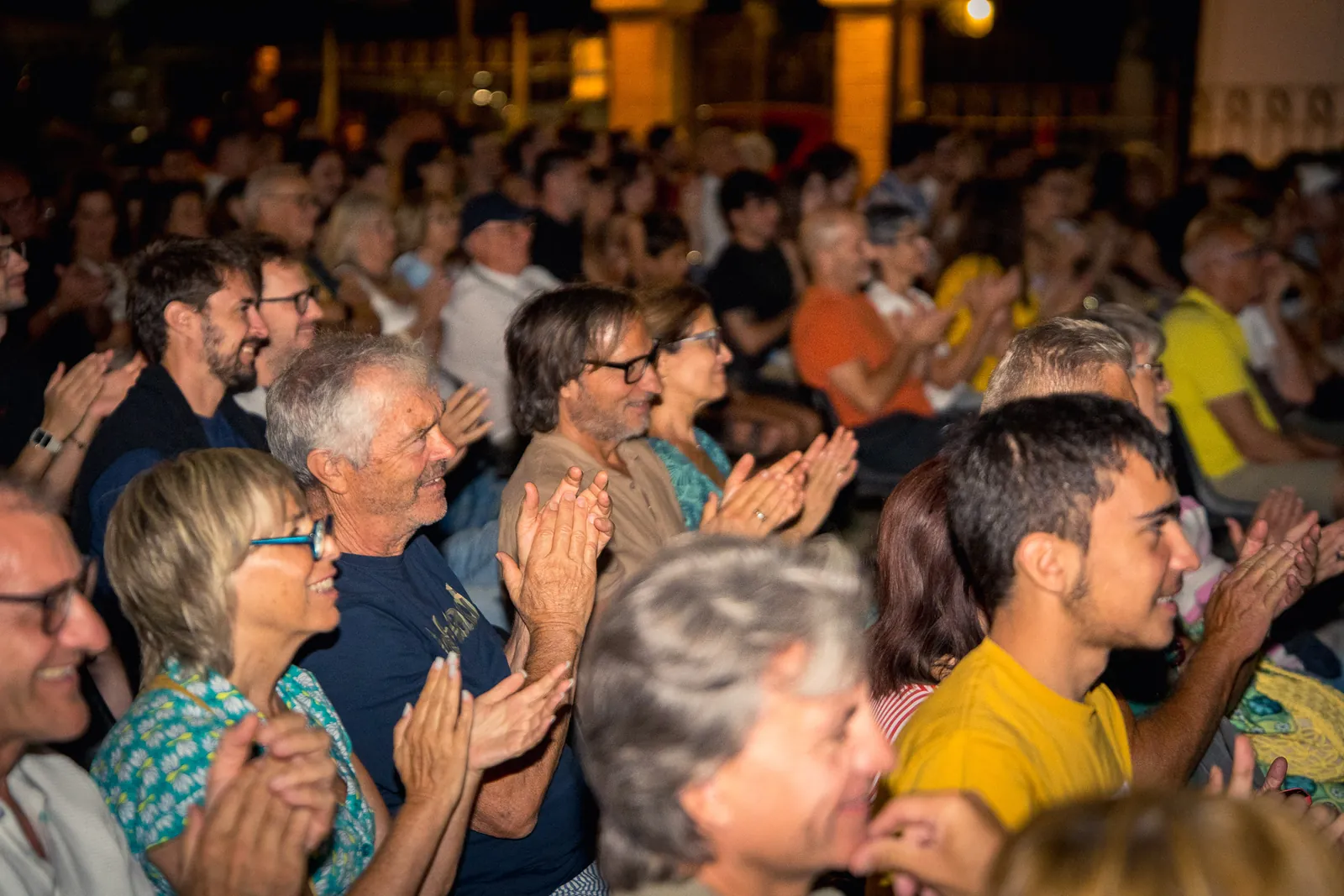 Il pubblico applaude nella sera, illuminato dalle luci del festival