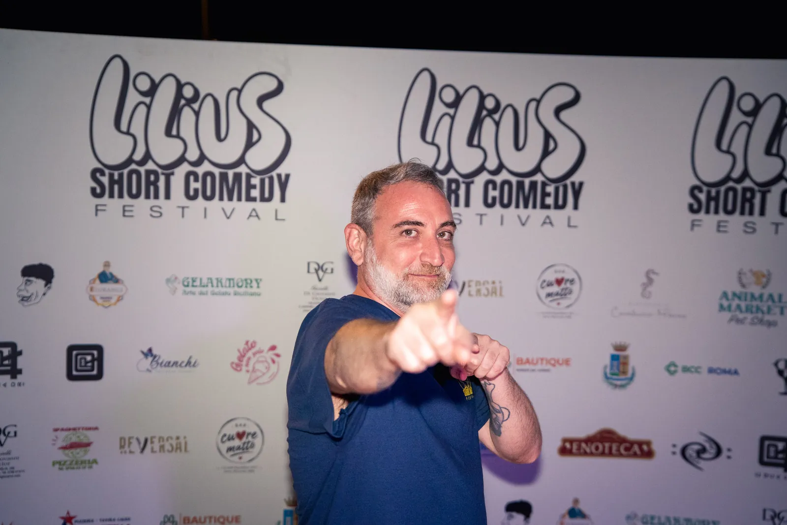 Uno spettatore punta il dito verso l'obiettivo sorridendo, davanti al backdrop del festival
