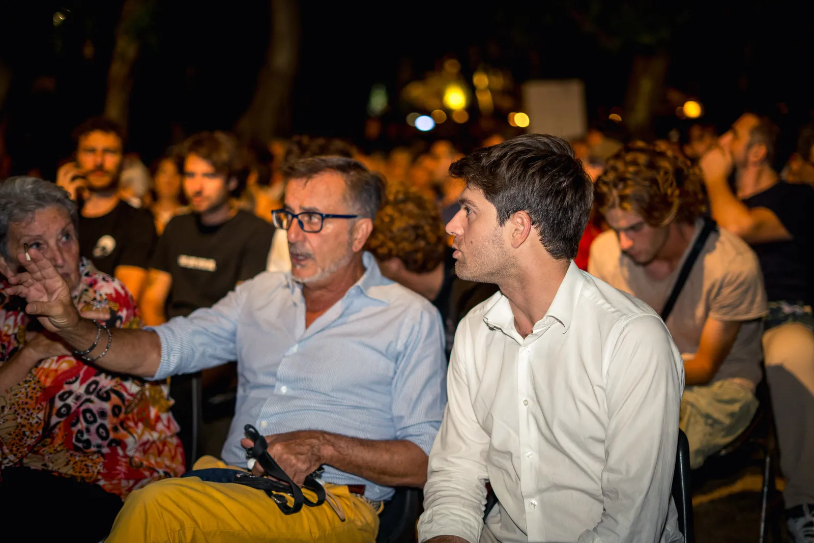 Il pubblico applaude, con due spettatori che chiacchierano tra la folla