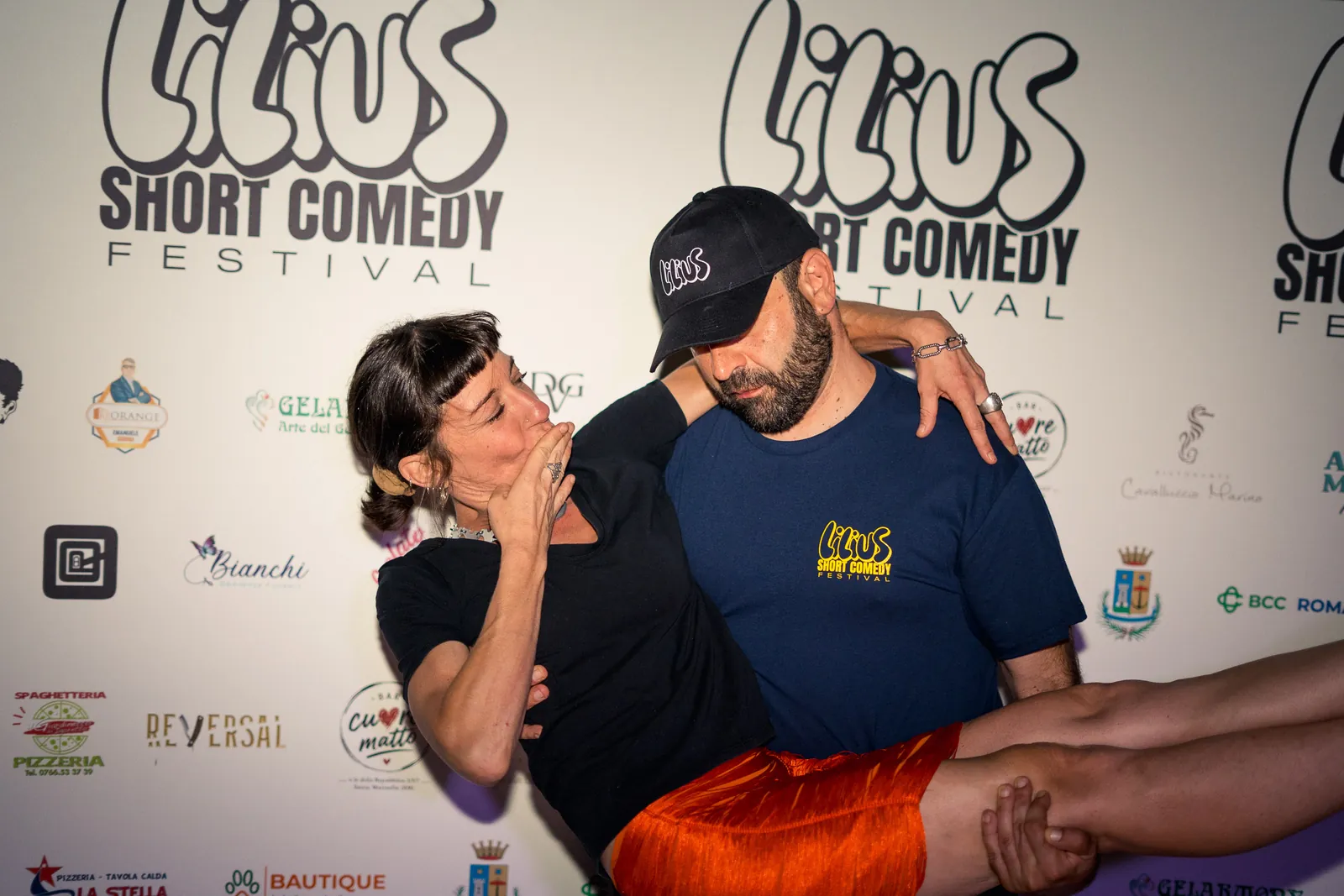 Due amici abbracciati in posa scherzosa davanti al backdrop del festival
