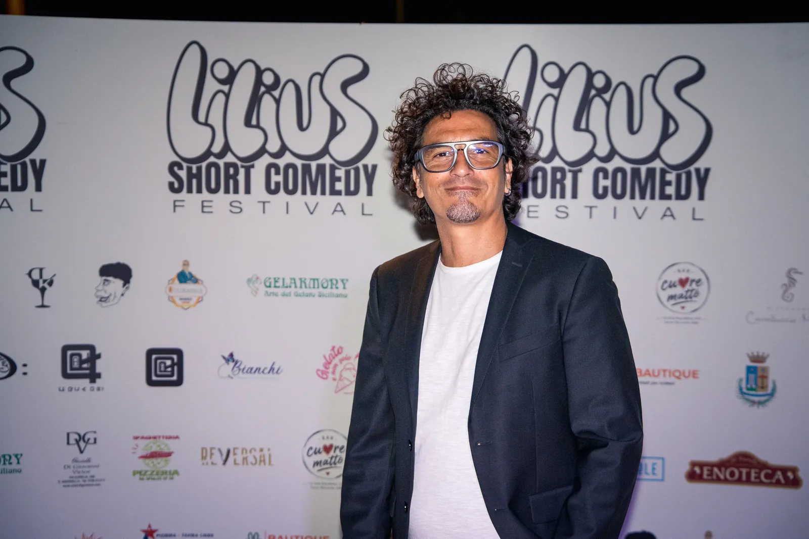 Ritratto di uno spettatore con giacca scura e capelli ricci davanti al backdrop del festival