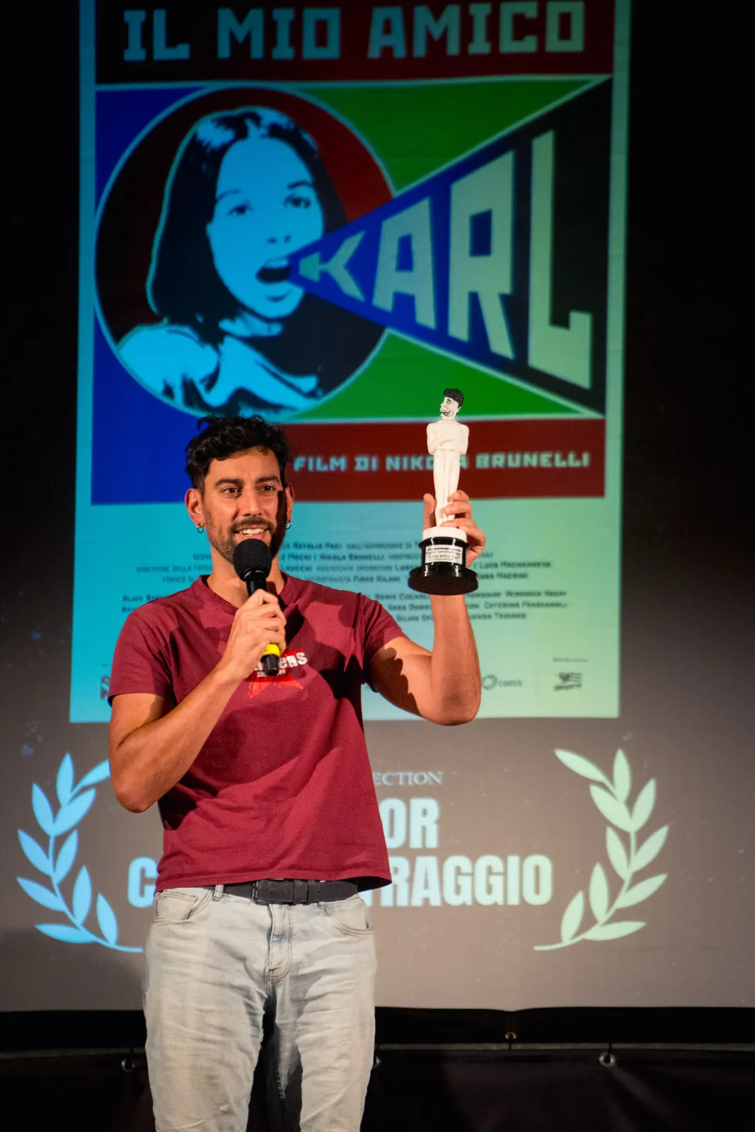 Il vincitore del Miglior Cortometraggio sul palco, davanti allo schermo di proiezione, con la locandina de Il mio amico Karl e due corone d'alloro